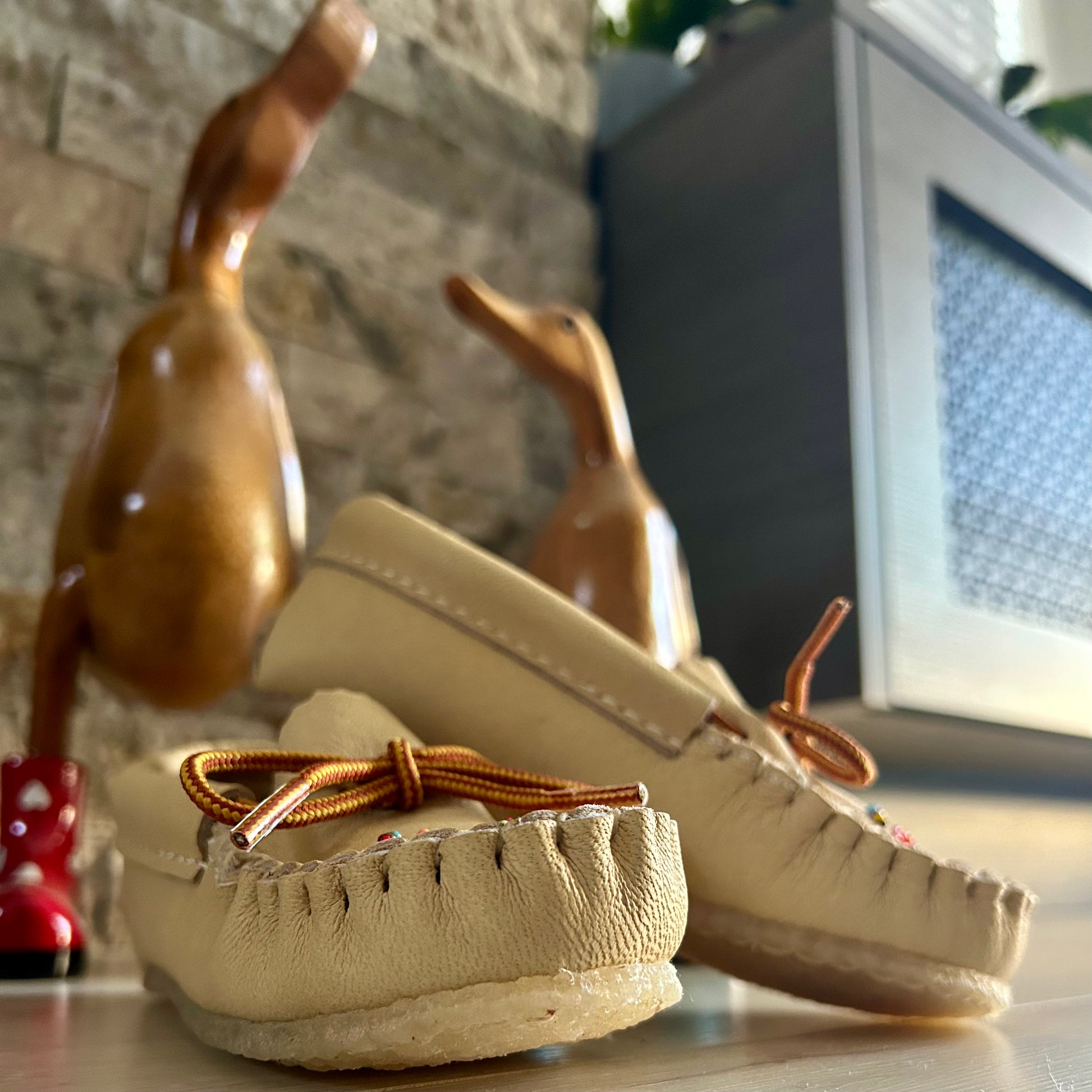 Pair of beige moccasins with brown laces on a surface with decorative elements in the background.