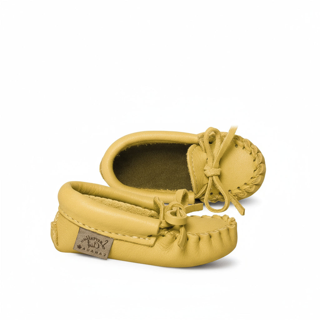 Pair of yellow baby moccasins with a visible brand label on a white background