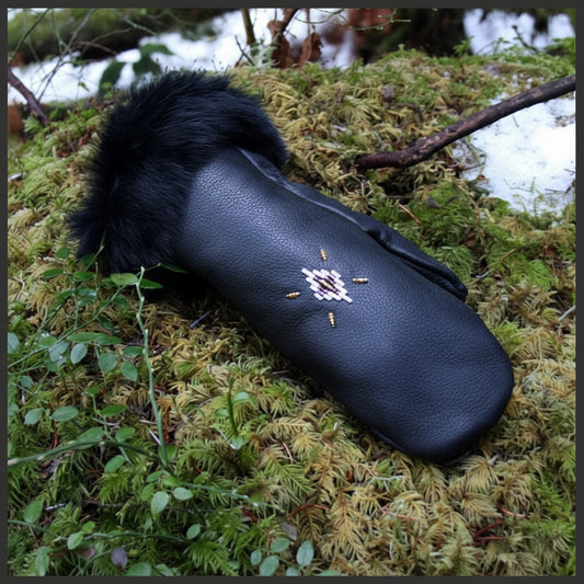 A black leather mitten with a fur cuff, featuring hand-beaded design with gold, purple, and pearl glass beads, resting on a bed of moss.