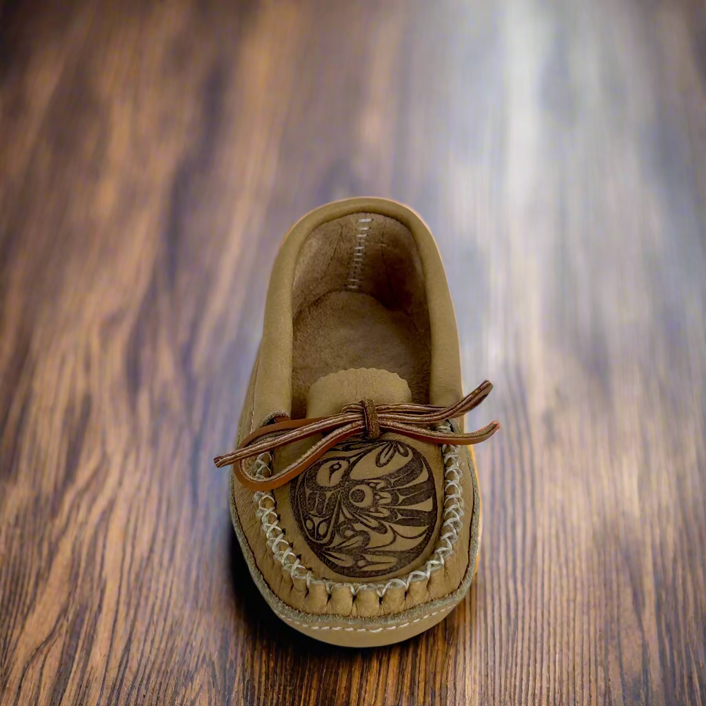 Tan moccasin shoe with a decorative design on a wooden surface