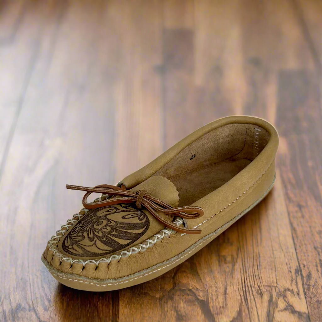 Tan moccasin shoe with brown leather details on a wooden surface