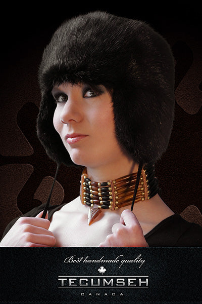 Person wearing a black fur hat with a dark background, featuring the brand 'Tecumseh'.