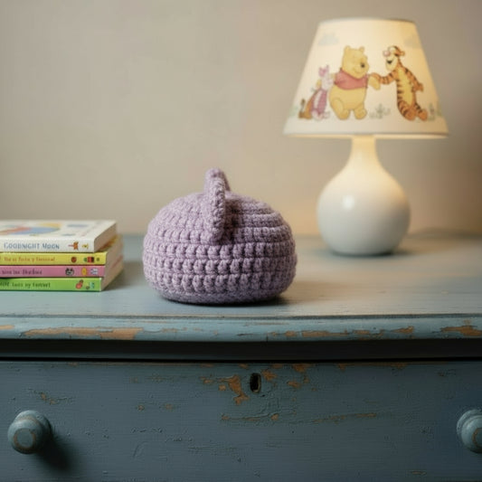 Crocheted beige baby beanie for newborn  on a wooden surface with folded towels in the background.