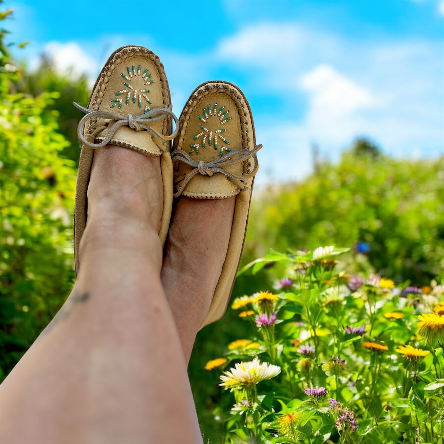 Person wearing tan loafers with decorative sole design, standing on a grassy area with flowers.