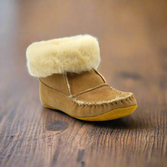 Tan sheepskin slipper with merino wool lining on a hardwood floor 