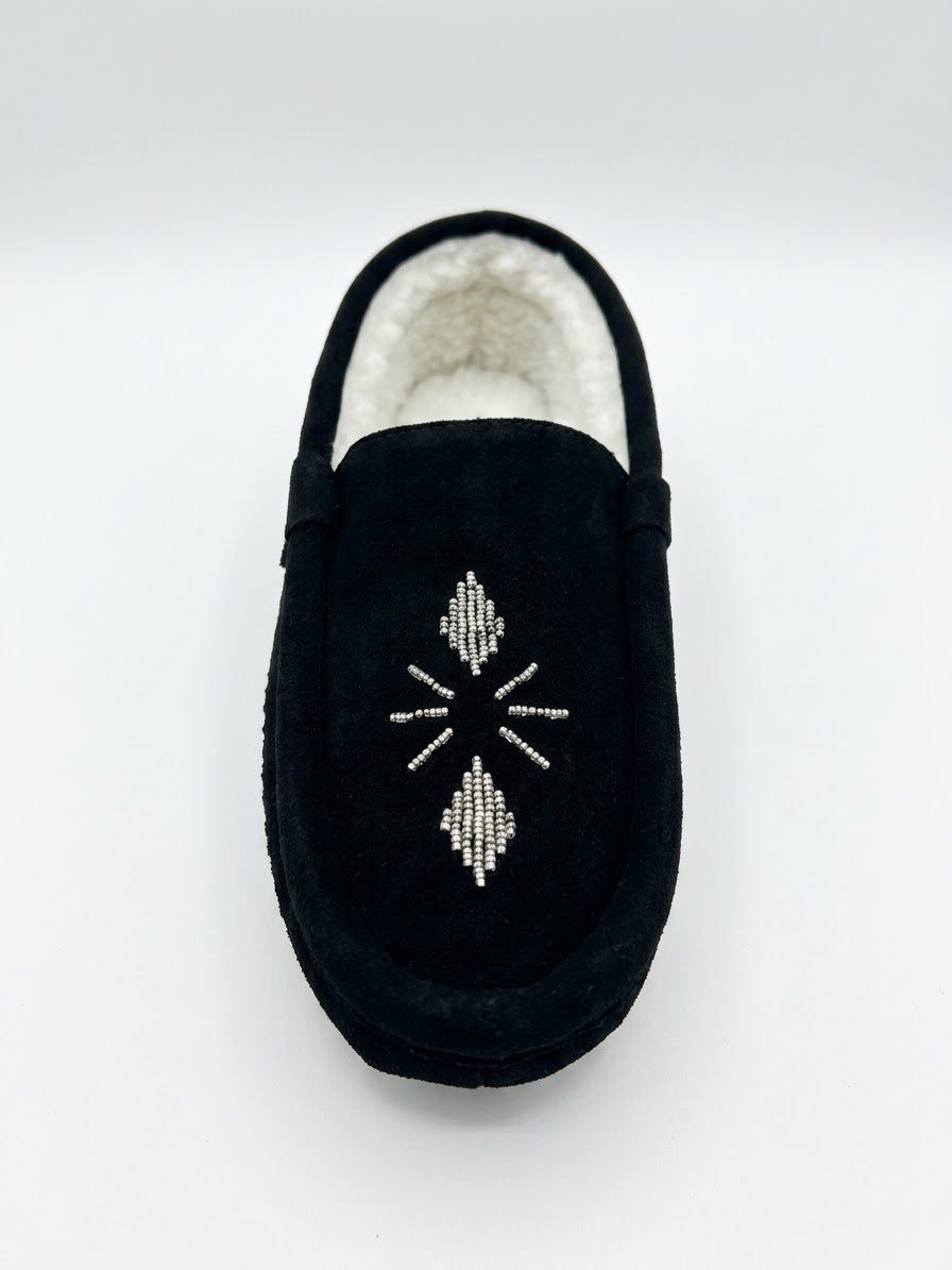 A single black suede moccasin slipper with a white sherpa lining and a white beaded geometric diamond pattern on the side, shown against a plain white background.