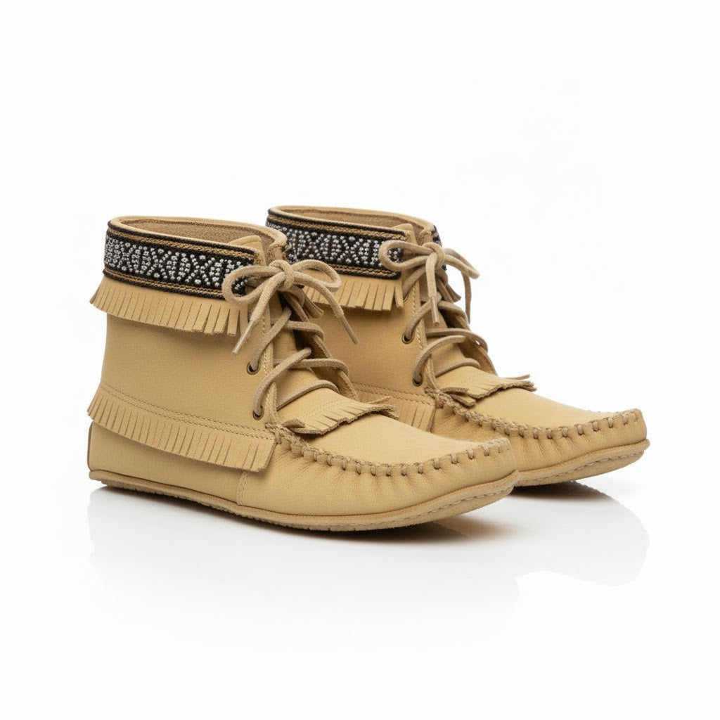 Pair of tan moccasin boots with fringes and a decorative band on a white background
