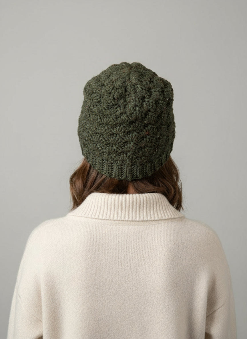 Person wearing a green knitted beanie and beige sweater on a gray background