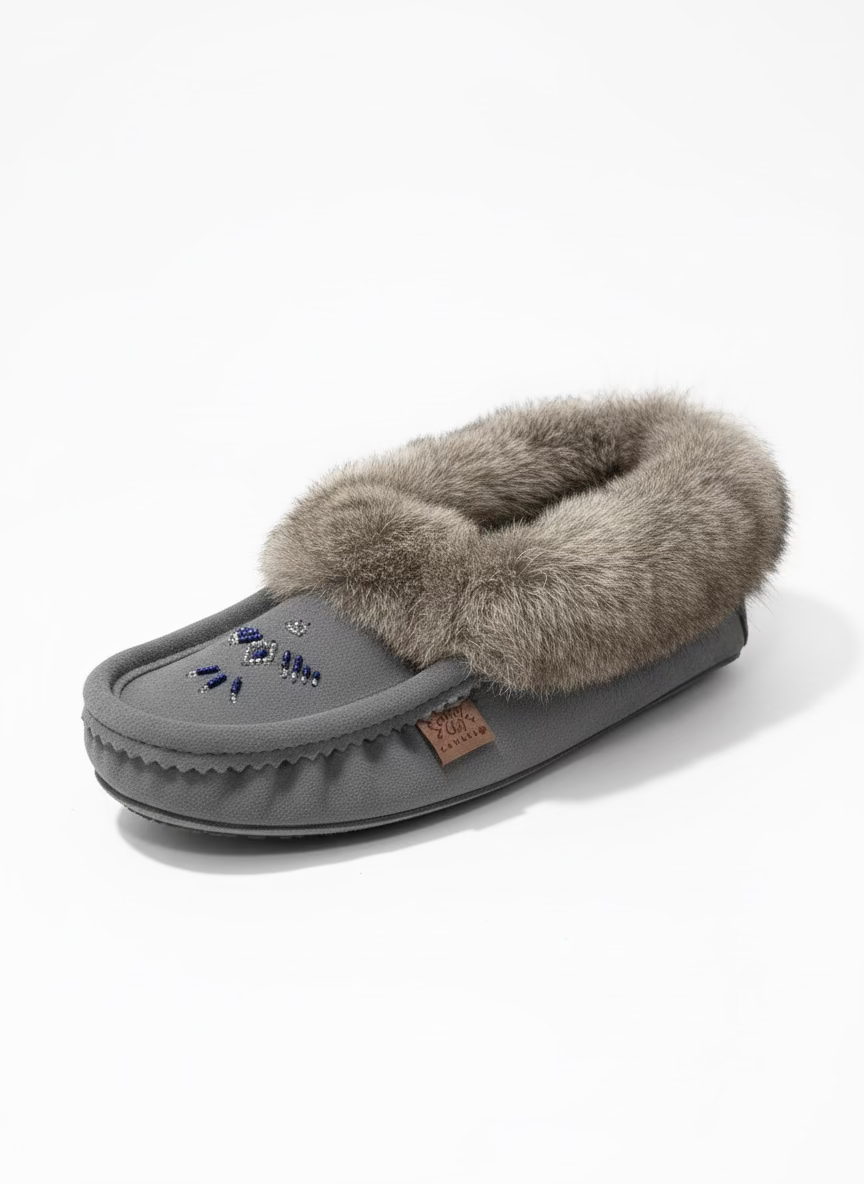 Gray fuzzy slipper with a brand label on a white surface, with an open box in the background.