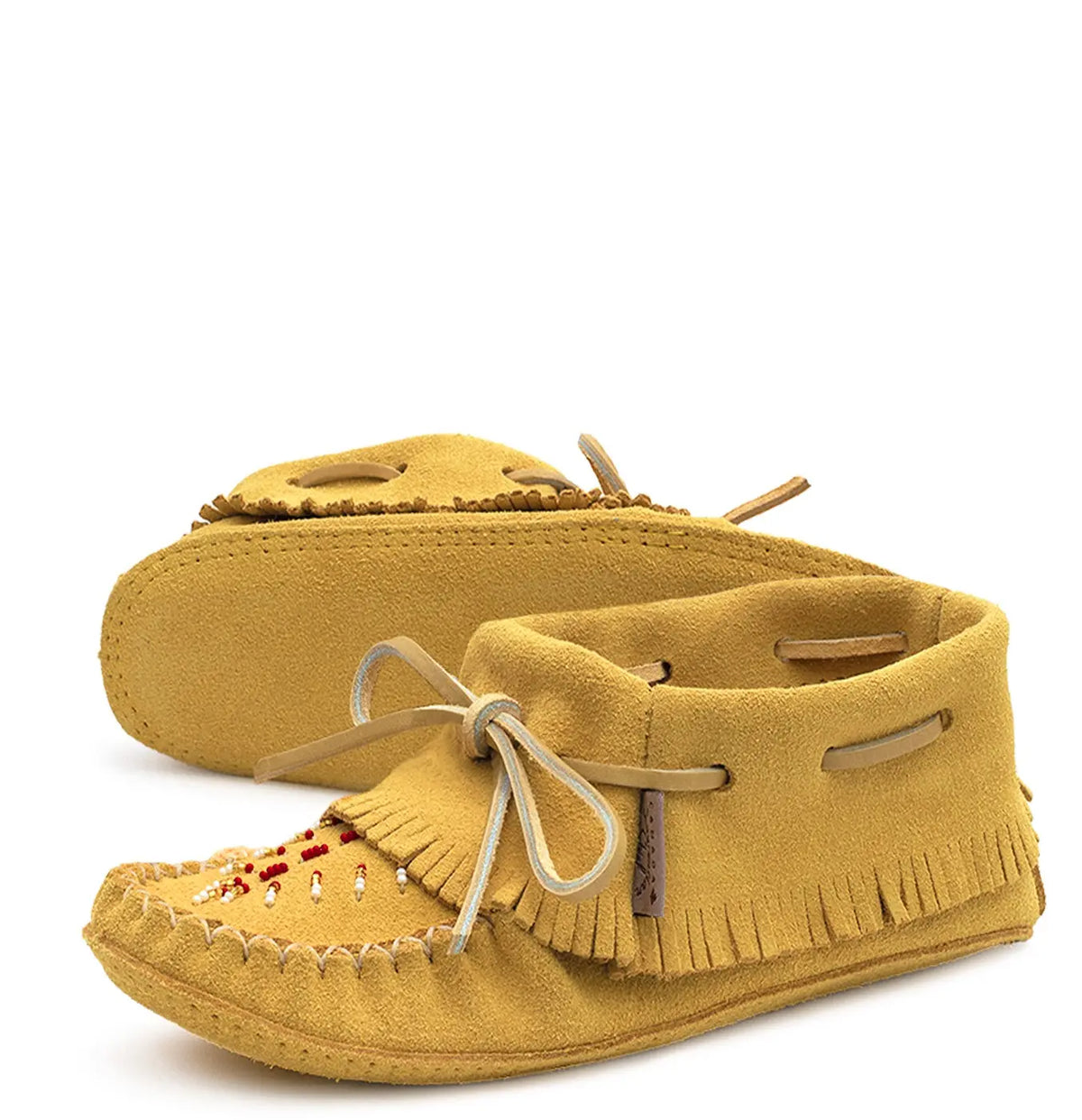 A pair of mustard yellow suede moccasin-style slippers with fringed toes, decorative beadwork, and cream-colored laces, shown on a white background.