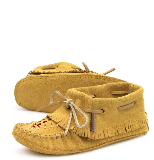 A pair of mustard yellow suede moccasin-style slippers with fringed toes, decorative beadwork, and cream-colored laces, shown on a white background.