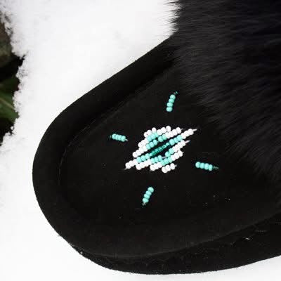 Black shoe with white and green bead design on a snowy background