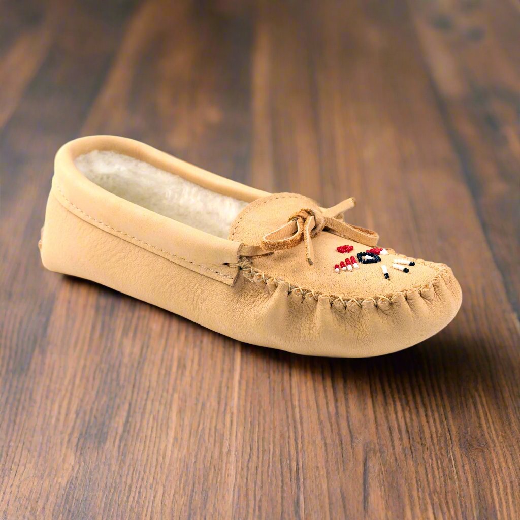 Beige moccasin slipper with embroidered details on a wooden surface