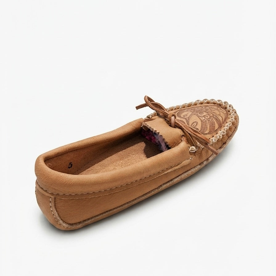 A single tan leather moccasin loafer shown from a three-quarters angle on a light gray background. The shoe features a tan leather upper, a braided jute trim around the toe, a decorative embroidered pattern on the vamp, and a matching tan leather tie-moccasin bow.