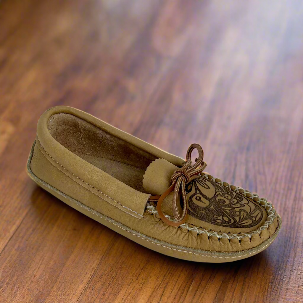 Tan moccasin shoe with decorative vamp on a hardwood floor