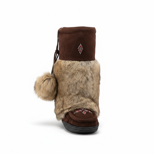 Brown fur boot with pom-pom on a snowy ground with trees in the background