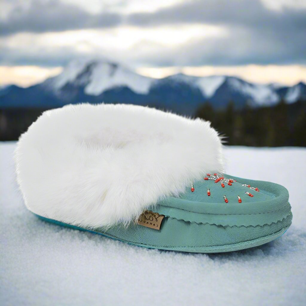 Teal slipper with white fur on a snowy surface with mountains in the background