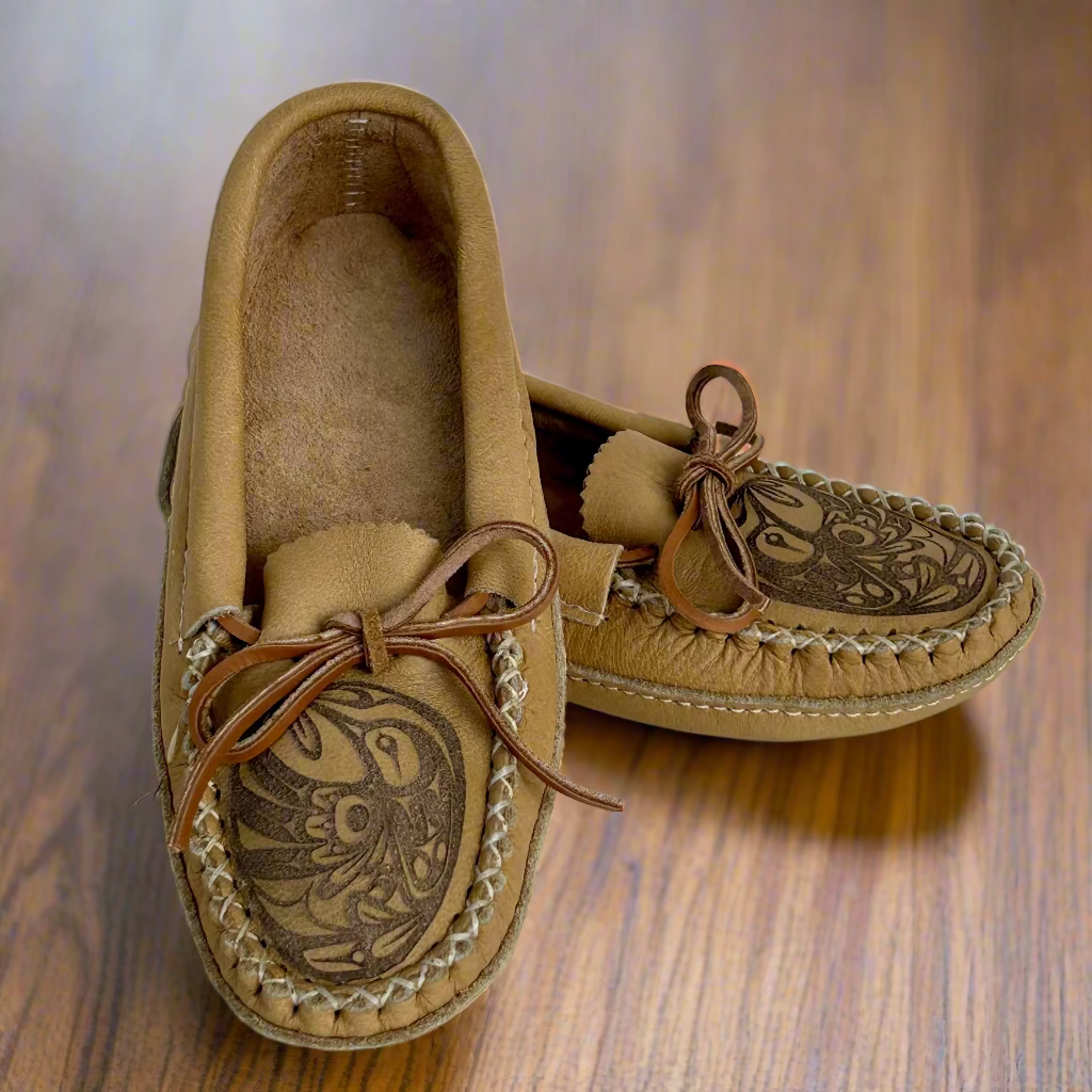 Pair of tan moccasin shoes with intricate designs on a wooden surface