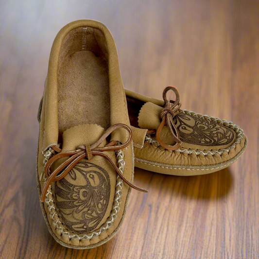 Pair of tan moccasin shoes with intricate designs on a wooden surface