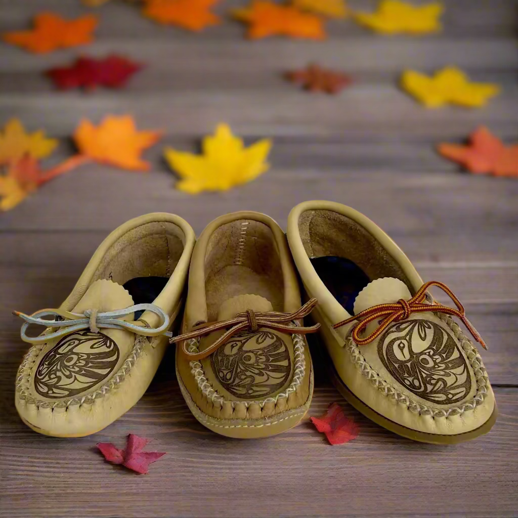 Three pairs of tan moccasin shoes with decorative designs on a wooden surface.